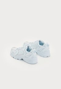 Vaaleansiniset urheilukengät, joissa on teksturoitu verkkopinta, pilkullinen kuvio, pehmustettu pohja ja näyttävä "N"-logo sivuilla.