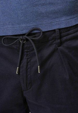 Pantalones cortos de algodón azul marino con cintura ajustable y puntas de metal plateadas, exhibidos sobre una camisa azul. Tejido texturizado visible.