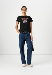 Svart bomull t-skjorte med rødt trekantlogo, kombinert med høyt liv mørk denim jeans og hvite åpne sandaler.
