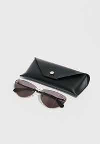 Gafas de sol negras con forma de ojo de gato y lentes oscuras junto a un estuche triangular de cuero negro con cierre de botón plateado.