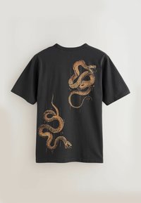 T-shirt noir à manches courtes avec deux serpents dorés stylisés imprimés au dos, l'un près du coin supérieur droit et l'autre près du coin inférieur gauche.