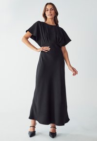 Robe noire, longue jusqu'au sol, avec des manches courtes et larges et une taille cintrée. Tissu lisse avec une silhouette drapée et un ourlet en forme de feston.