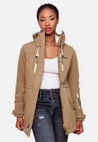 Beige softshell jacket with a hood, designed with zippered pockets, drawstring details, and a smooth, textured finish. Worn over a white top.