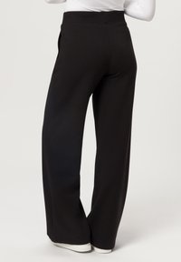 Schwarze weit geschnittene Hose aus weichem Material mit hohem Bund, seitlichen Taschen und glatter Textur, kombiniert mit weißen Sneakern.