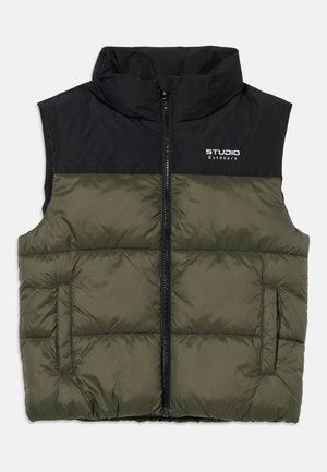 Veste sans manches matelassée avec fermeture éclair sur le devant, corps vert olive, épaules noires et logo "STUDIO Outdoors" sur la poitrine.