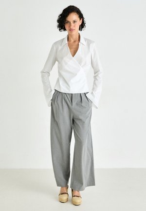 Balta apykaklė blusa, derinama su pilkomis dryžuotomis plačiomis kelnėmis ir rusvomis platforminėmis bateliais. Lygus audinys ir laisvas siluetas.