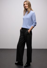 Jasnoniebieski sweter z prążkowanego dzianiny w zestawieniu z szerokimi spodniami w ciemnoszarym kolorze oraz czarnymi butami ze złotymi akcentami. Prosta i nowoczesna sylwetka.