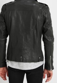 Veste en cuir noir avec une finition légèrement texturée, une quincaillerie en argent, des fermetures éclair aux poignets des manches et une coupe droite.