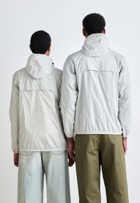 Light gray hooded jackets with elastic cuffs and hem, worn by two figures, paired with faded denim and olive green trousers.