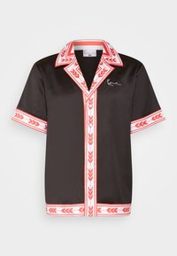 Black short-sleeve button-up shirt with red and white patterned trim on collar, sleeves, front, and hem, featuring a small white signature on the chest.