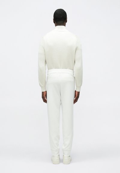 Μαλακό λευκό πλεκτό πουλόβερ με ψηλό λαιμό και ριμπ υφή. Συνδυασμένο με λευκά τζόγκερς που ταιριάζουν, με εφαρμοστή γραμμή και ελαστικές μανσέτες.
