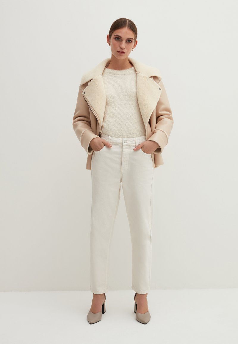 Beige Kunstlederjacke mit Schaffellkragen, cremefarbener Strickpullover, weiße hochtaillierte Jeans und beigefarbene Absatzschuhe. Minimalistisches Design.