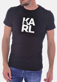 T-shirt nera in cotone con maniche corte. Presenta una stampa grafica frontale in bianco con la parola "KARL" e una silhouette.