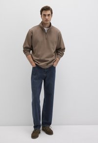 Beige pullover with zip neck, paired with blue jeans and brown shoes. The pullover features long sleeves and ribbed cuffs.