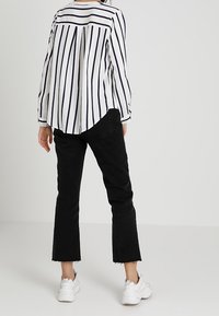 Blouse rayée avec des rayures verticales bleu marine et blanches, manches longues et un pli au dos. Associée à un jeans noir court et des baskets blanches.
