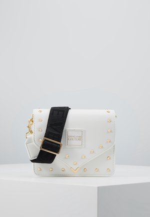 White leather crossbody bag with gold studs, a black adjustable strap, and Versace Jeans Couture logo on front flap.