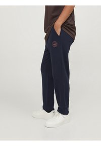 Navy blue sweatpants made of soft fabric with a relaxed fit. Features side pockets and a circular logo detail in pink on the left leg.