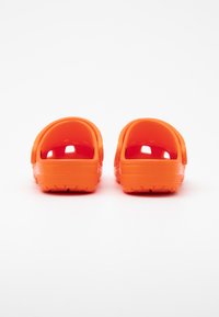 Lysorange träskor med en strukturerad yta, öppen häl och utskärningar för ventilation. Gummimaterial och vågig sula för grepp.