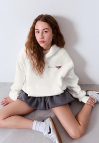 Fehér kapucnis pulóver "Disney Pixar Cars" logóval, szürke szoknyával fehér pöttyökkel és ezüst sportcipővel párosítva. Puha, hétköznapi anyag.