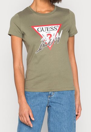T-shirt en coton vert olive avec un logo en forme de triangle rouge portant "GUESS®" et "1981" en sequins argentés ; design ajusté avec des manches courtes.