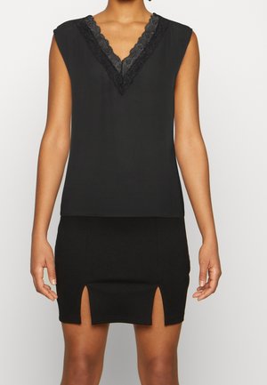 Vrouw draagt een mouwloos zwart topje met een kanten V-hals en een zwarte minirok met twee vooraan gespen.