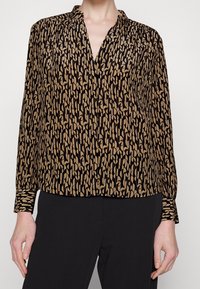 Long-sleeve blouse in black and beige with abstract pattern, lightweight fabric, v-neck, and buttoned cuffs. Designed for a relaxed fit.