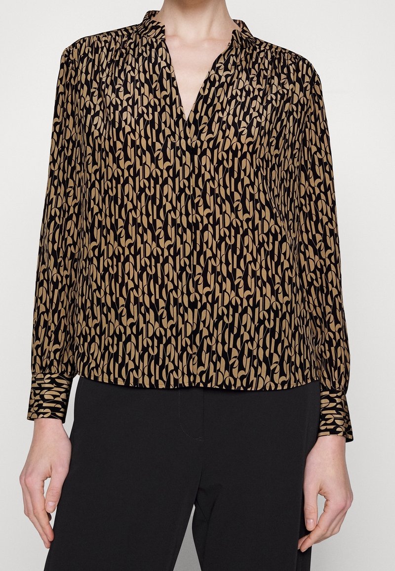 Long-sleeve blouse in black and beige with abstract pattern, lightweight fabric, v-neck, and buttoned cuffs. Designed for a relaxed fit.