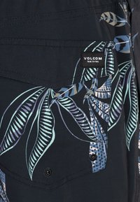 Camisa negra con un patrón de hojas tropicales en tonos azules y verdes. Presenta una etiqueta de Volcom y acentos de botones en una tela texturizada.