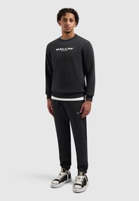 Zwarte sweatshirt met het logo "BALLIN.", gecombineerd met bijpassende zwarte joggers; voorzien van geribbelde manchetten, zijzakken en accenten van witte sneakers.
