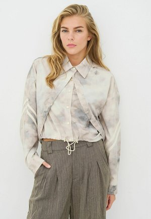 Leichtes, langärmeliges Batikshirt mit Kragen, tailliertem Bund und dekorativen Streifen; kombiniert mit grauen, gestreiften, hoch taillierten Hosen.