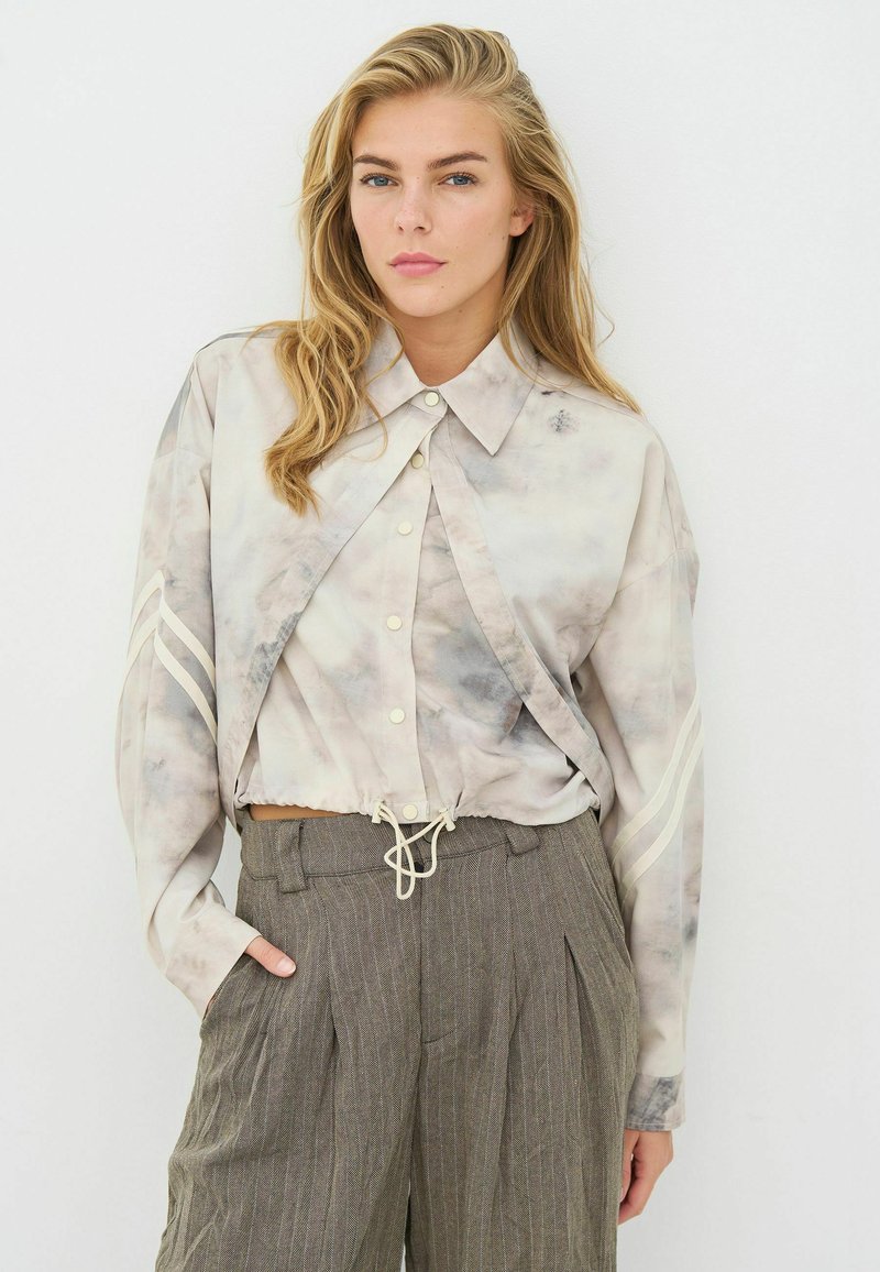 Maglietta leggera a maniche lunghe con effetto tie-dye, collo con risvolto, vita aderente e strisce decorative; abbinata a pantaloni grigi a righe, a vita alta.