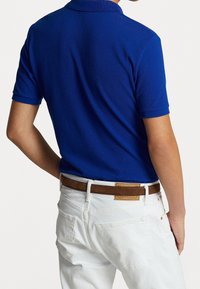 Blå pikétröja med korta ärmar, tillverkad av mjukt tyg. Kombinerad med vita jeans och ett brunt läderbälte med en etikett.