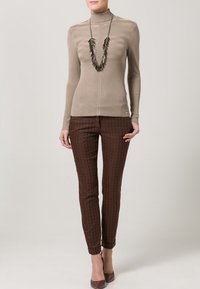Maglione beige a collo alto a coste abbinato a pantaloni slim-fit marroni con motivo. Gli accessori includono una lunga collana scura.