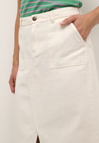 Beige Jeansrock mit einem vorderen Schlitz, zwei Seitentaschen und einem Knopfverschluss. Der Stoff hat eine glatte Textur mit sichtbaren Nähdetails.