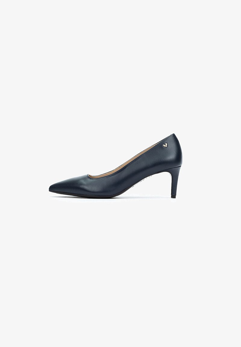 Zapato de charol azul marino con punta afilada y tacón cónico, que presenta un sutil detalle del logo dorado en el costado exterior. Textura suave.