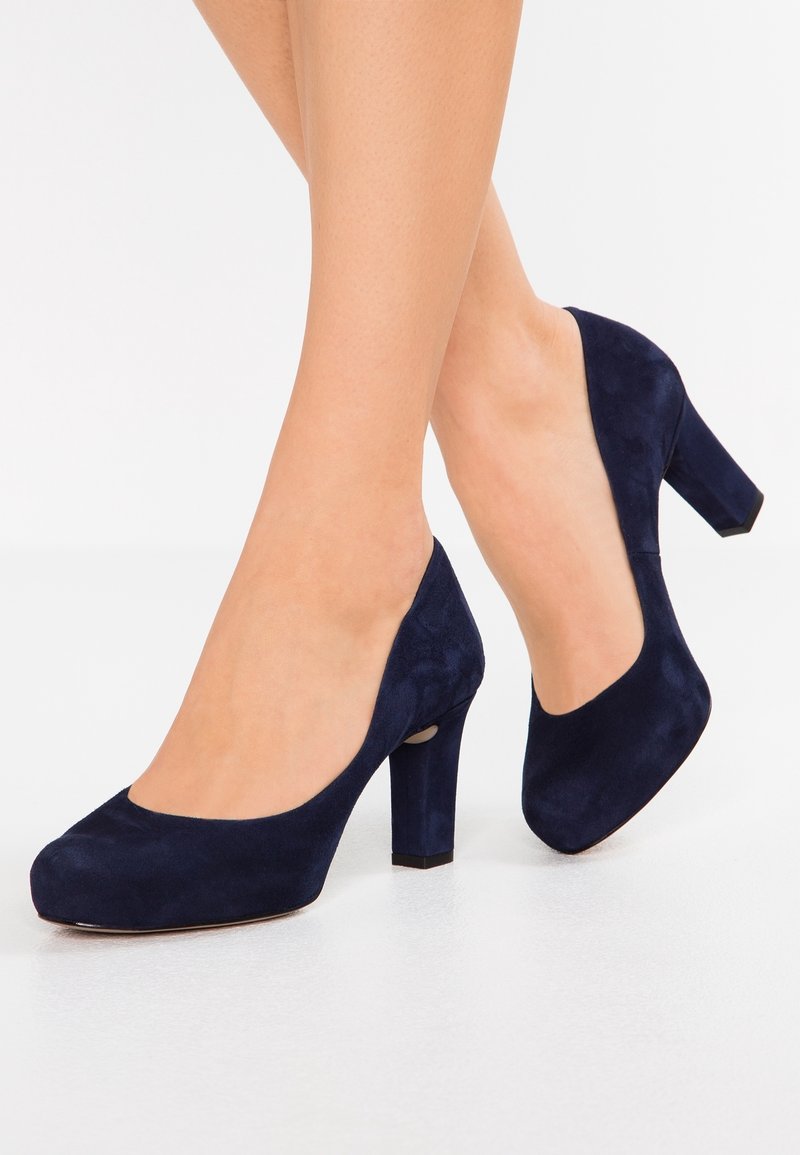 Escarpins en suède bleu marine à talon haut avec un bout rond et un talon épais, présentant une texture lisse et des détails de design minimalistes.