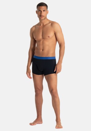Black boxer briefs with a blue waistband, featuring a snug fit and soft texture. Model stands with a neutral posture, barefoot, and shirtless.