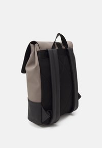 Sac à dos avec un mélange de matériaux gris et noirs, doté de bretelles en mesh texturé, d'un design à fermeture enroulable et d'un accent triangulaire à la base.