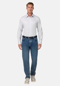 Weiß gestreiftes Button-Up-Hemd, blaue Jeans mit Gürtel und beigen Sneakern; klassischer Schnitt, strukturierter Stoff mit kontrastierenden Nähten.