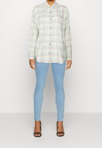 Camicia a maniche lunghe a quadri in verde chiaro e beige, con chiusura a bottoni, tasche sul petto e taglio rilassato, abbinata a jeans skinny.