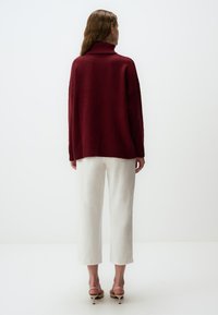 Bordeaux coltrui met een losse pasvorm, geribbelde manchetten en zoom. Gepaard met witte broek met wijde pijpen. Gladde textuur. Eenvoudig ontwerp.
