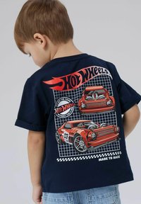 Tumši zila kokvilnas t-krekls ar sarkano auto grafiku, uzrakstu "Hot Wheels" un melnbaltu šaha rakstu.