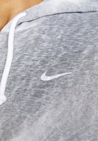 Jasnoszara bluza z kapturem z teksturowanym wzorem, białymi sznurkami i małym białym logo Nike w okolicy klatki piersiowej.