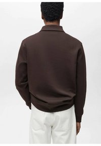 Pullover marrone con colletto, realizzato in un tessuto testurizzato, vestibilità comoda e polsini a costine. Indossato sopra pantaloni beige chiaro.