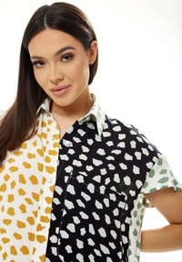 Button-up shirt featuring a color-block design in white with yellow spots, black with white spots, and green accents. Short sleeves and pocket detail.