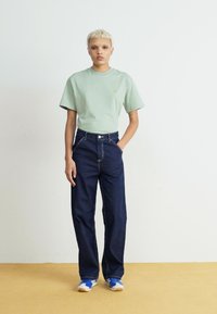 Ljusgrön bomullströja med korta ärmar och en liten logotyp, kombinerad med mörkblå denimbyxor med vida ben och kontrasterande sömmar.