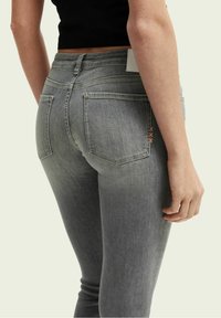 Jeans de mezclilla gris con bolsillos traseros, que presentan un ligero desvanecimiento, una cintura alta y costuras decorativas en melocotón en el bolsillo derecho.
