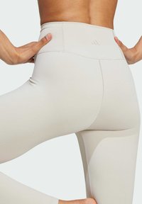 Beige högmidjade leggings med en slät textur, med sidopaneler och subtila sömnadsdetaljer. Stretchtyg förbättrar passform och komfort.