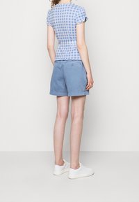 Top corto a maniche corte a quadretti blu e bianchi con bordi arruffati abbinato a pantaloni corti blu chiaro. Sneakers bianche completano l'outfit.