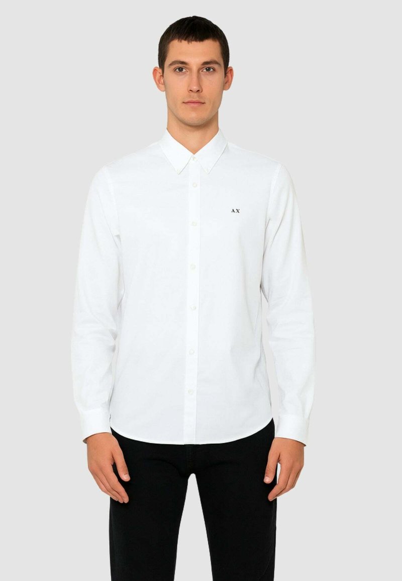 Camicia bianca a maniche lunghe realizzata in tessuto liscio con colletto classico, caratterizzata da un piccolo logo nero "AX" sul lato sinistro del petto.